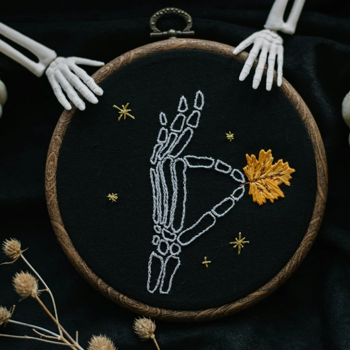 a hand embroidered picture of a skeleton holding a fall leaf